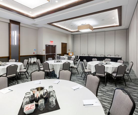 A large meeting room with round tables, white tablecloths, and gray chairs.