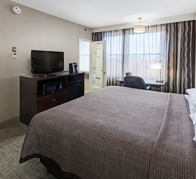 A wide-angle view of a hotel room with a large bed, TV, desk, and window.