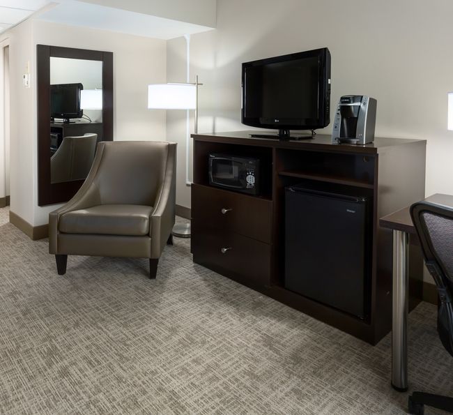 A hotel room with a chair, TV, fridge, microwave, and coffee maker.