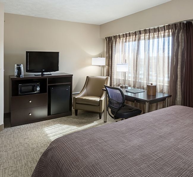 A wide view of a hotel room with a bed, desk, chair, and TV.