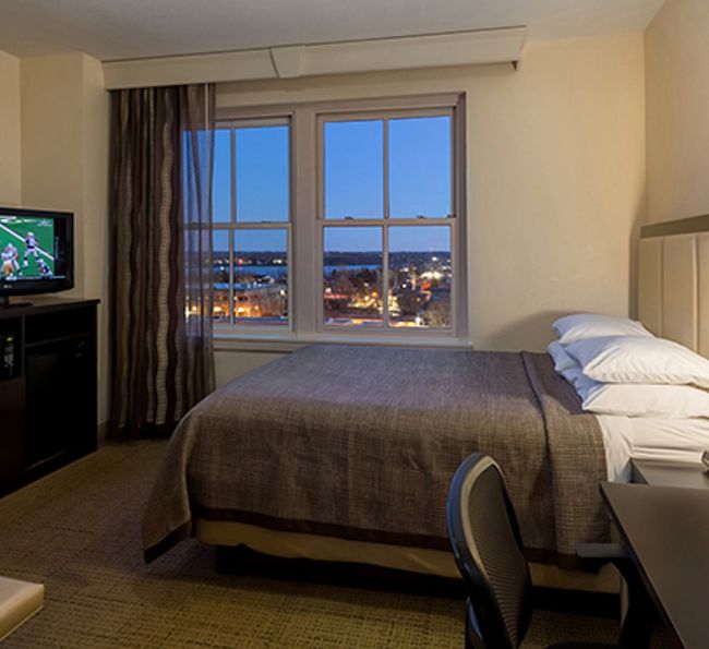 A hotel room with a bed, TV, and city view