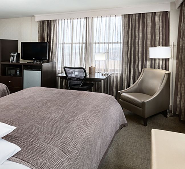 A hotel room with a bed, desk, chair, and TV in front of a window.