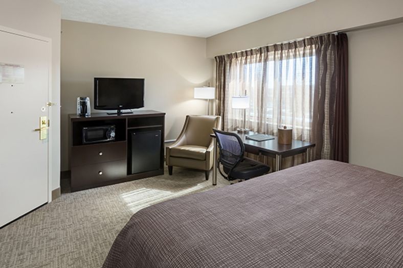 A hotel room with a bed, desk, TV, microwave, and mini-fridge.